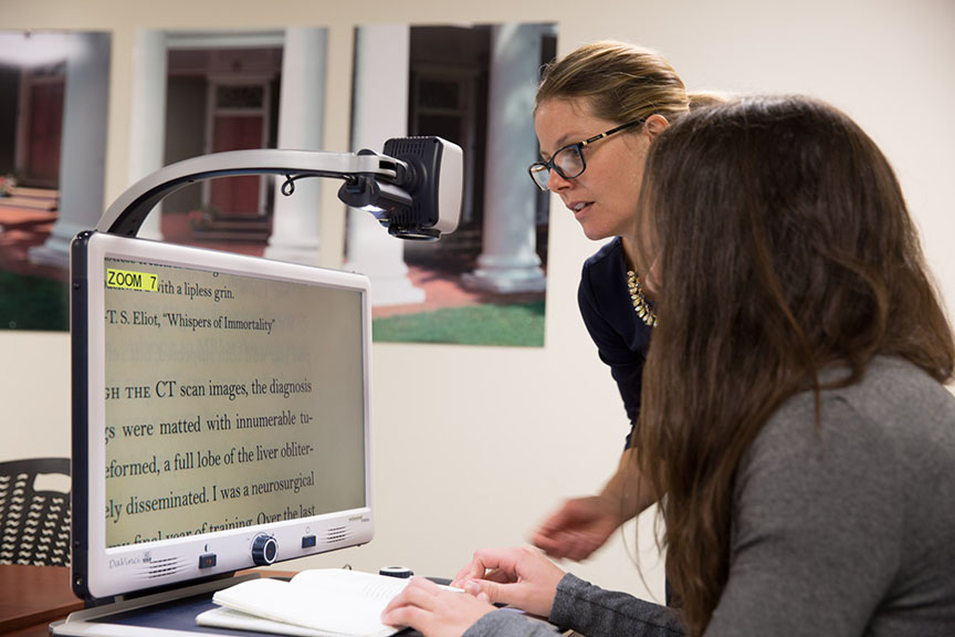 Two people are looking at a screen of a video magnifier device, projecting an image of a textbook page.