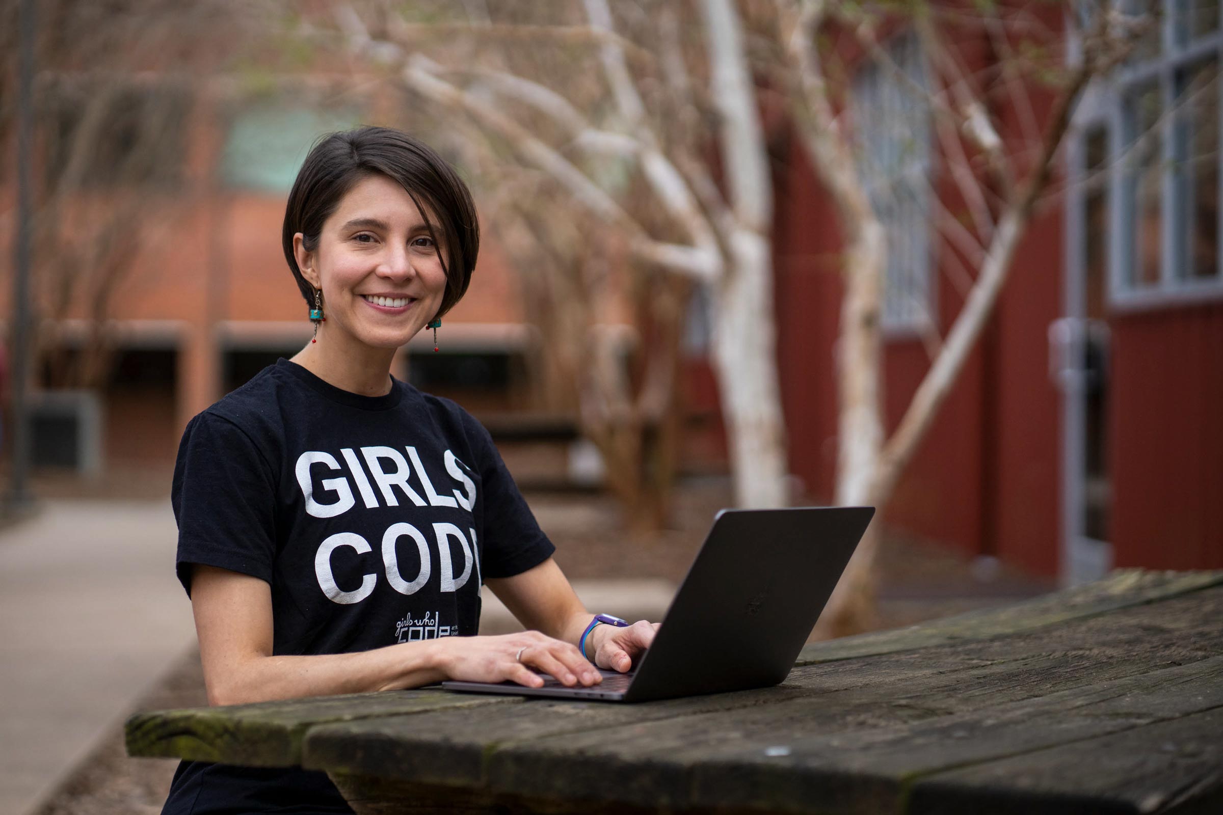 photo of a woman with short black hair and a black shirt sitting at a table with a laptop
